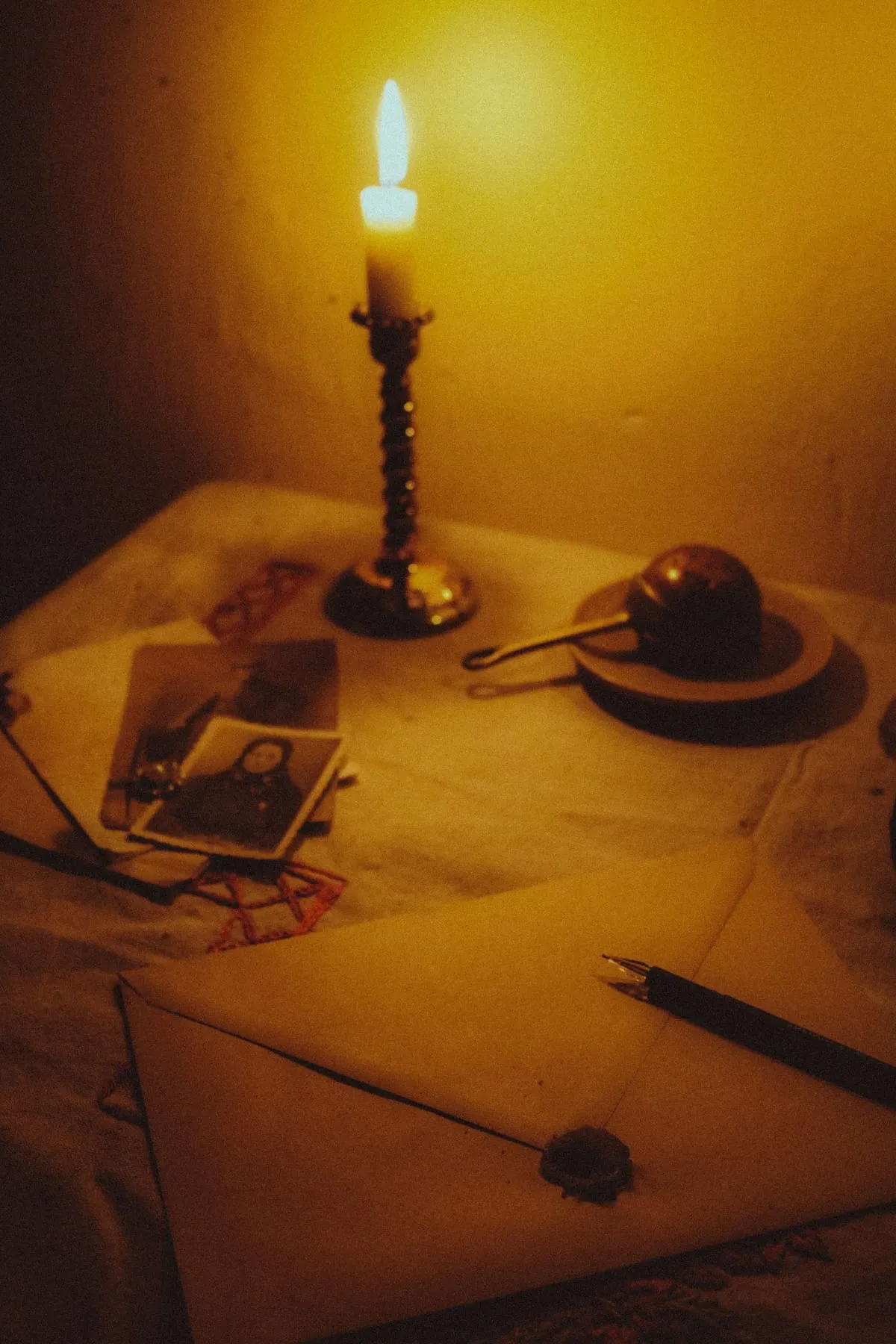 Una espelma encesa al costat de fotografies antigues, una carta segellada i una ploma