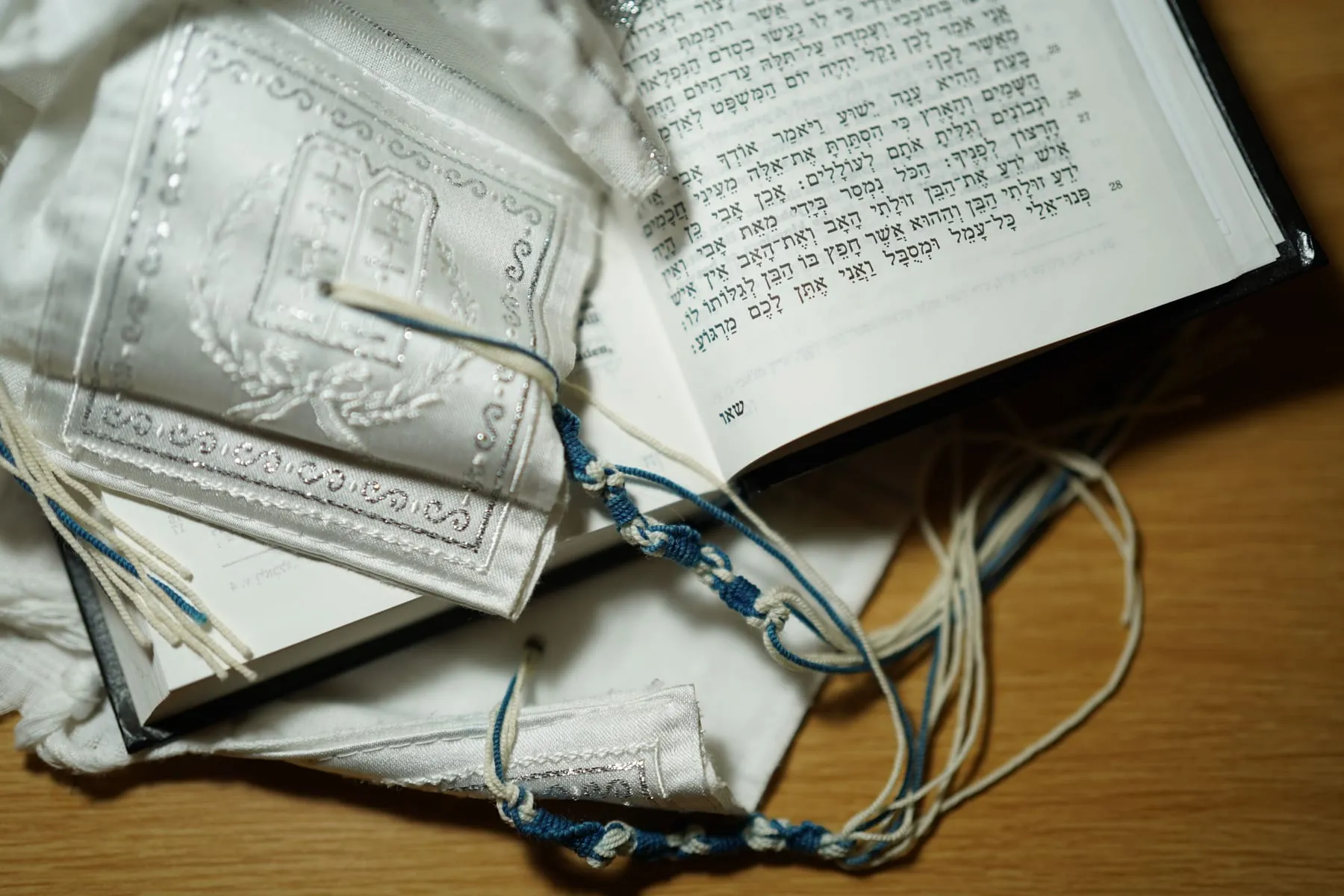 Llibre d’oracions obert amb text en hebreu al costat d’un mantell ritual