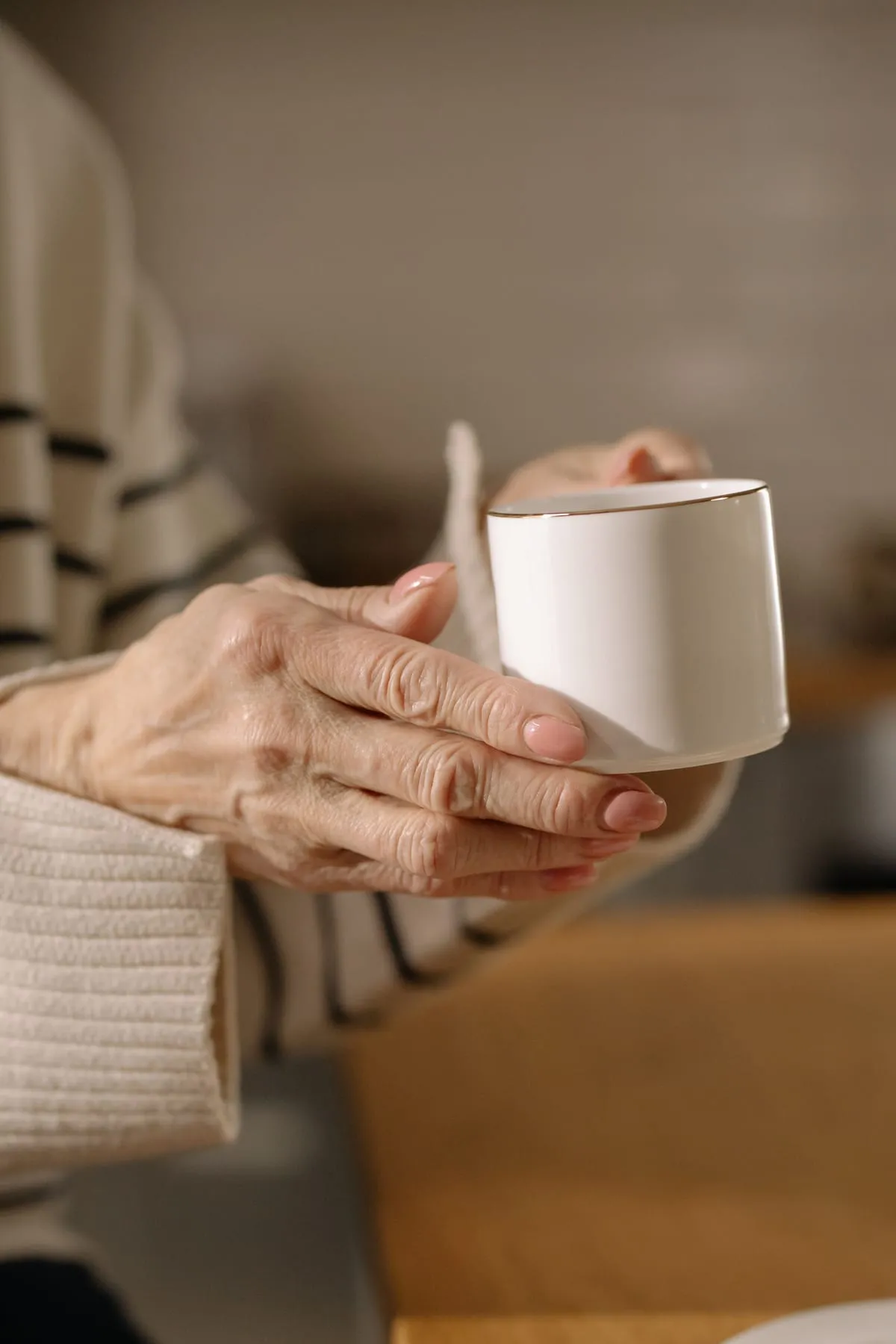 Mans d’una persona gran sostenint una tassa blanca a la cuina