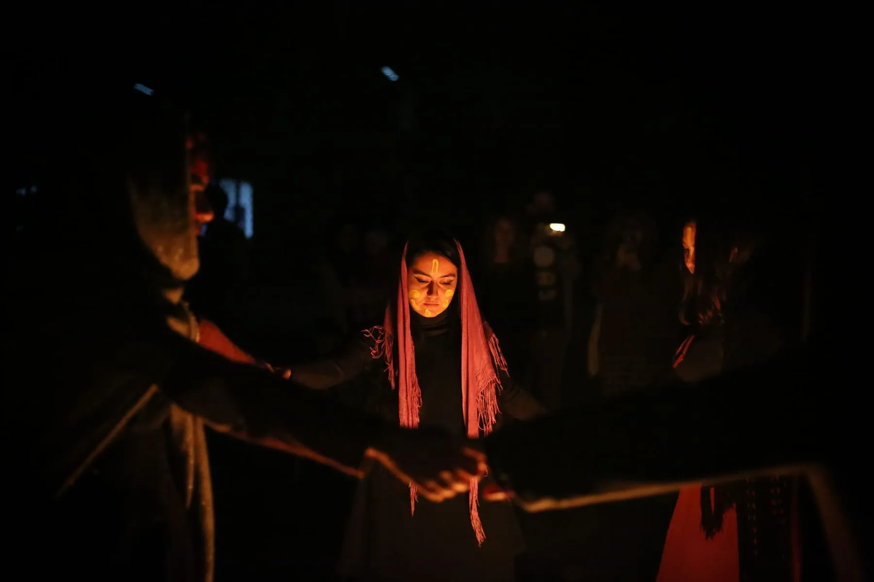 Dones amb les mans unides al voltant d’un foc durant un ritual nocturn