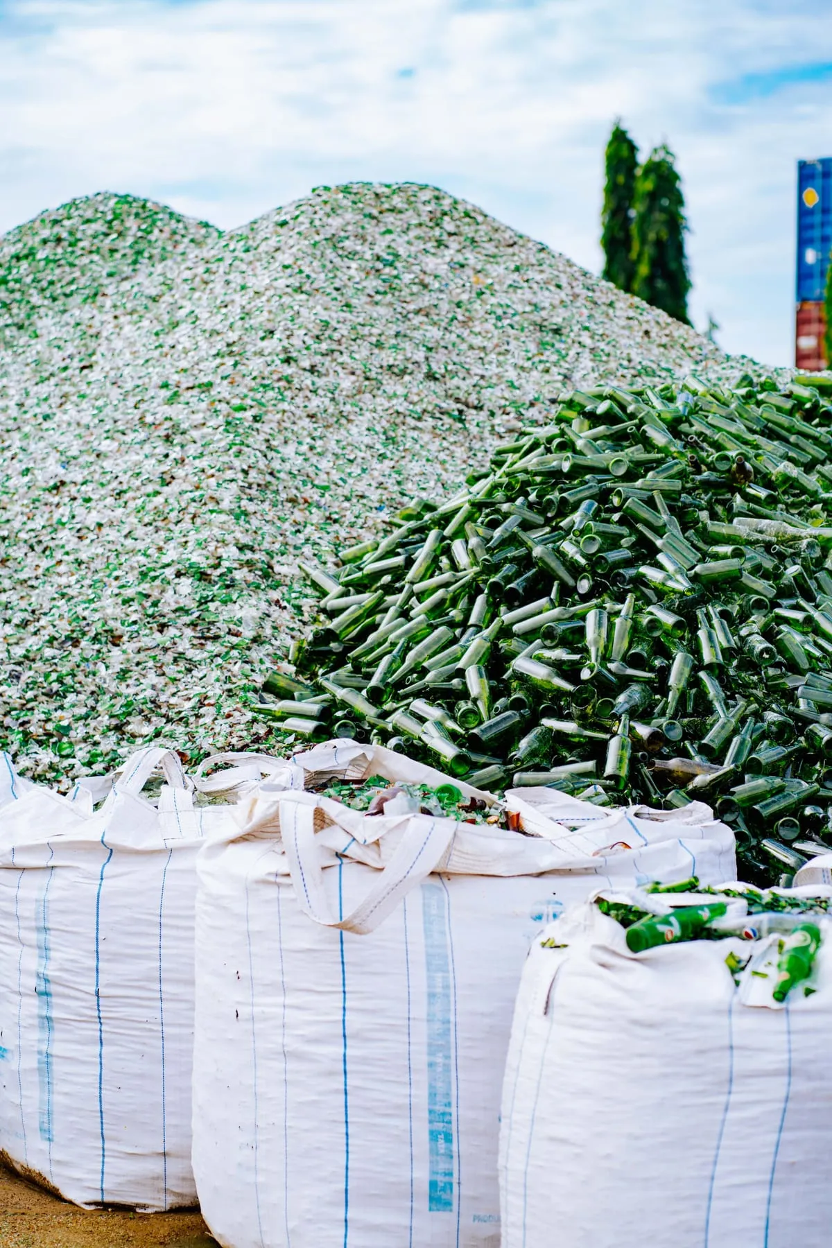 Sacs i munts de vidre triturat i ampolles verdes en una planta de reciclatge